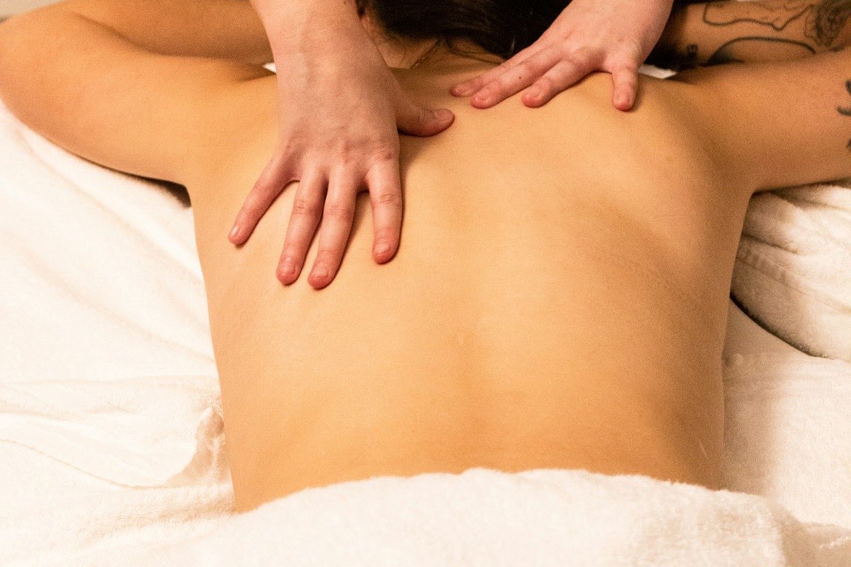 A therapist with both hands on the shoulders and upper back of a person lying on a made-up treatment table.